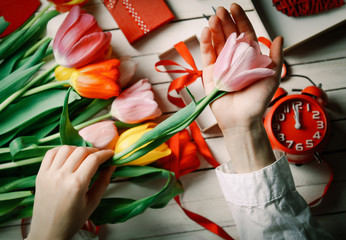 Female hands are holding a tulip flower before wrapping on white wooden background