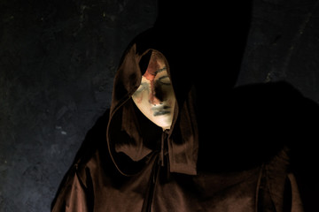 Hooded figure looms creepily by a black wall