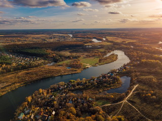Fototapeta na wymiar Aerial view of rural landscape in autumn sunset. Small village houses, river, autumn trees, farm fields from drone point of view