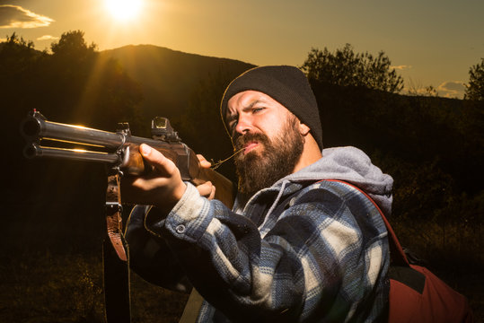 Bearded hunter man holding gun and walking in forest. Rifle Hunter Silhouetted in Beautiful Sunset. Autunm hunting. Mountain hunting. Barrel of a gun.
