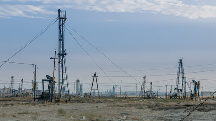 Desertous industrial landscape with oil pumps and rich modern city in background