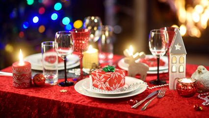 Beautiful table setting for Christmas party or New Year celebration at home. Cozy room with a fireplace and Christmas tree in a background.