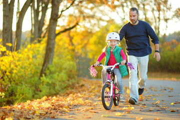 Happy father teaching his little daughter to ride a bicycle. Child learning to ride a bike. - obrazy, fototapety, plakaty
