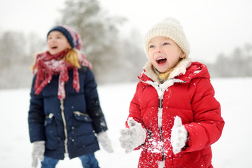 Two adorable little girls having fun together in beautiful winter park. Beautiful sisters playing...