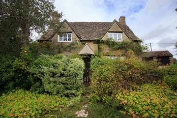 Fototapeta na wymiar Old English house in countryside with lush bushes covering path to entry gate