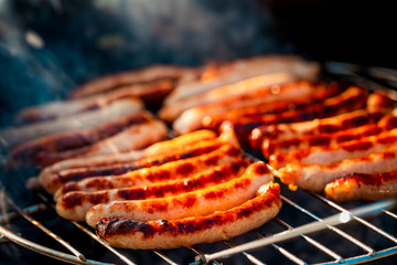 BBQ with fiery sausages on the grill outdoor picnic. Spending time together with the family at the grill. Social meetings, friends. Juicy and well-grilled sausages