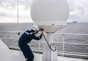 Marine service technician or serviceman repairing VSAT terminal on deck of vessel or ship. He is...