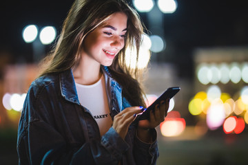 Young Girl holding in hands on blank screen tablet on background illumination glow bokeh light in night city.