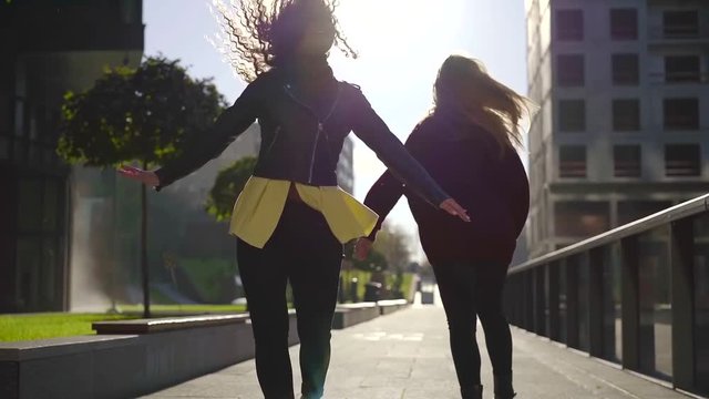 Two girlfriends kumping spinning and whirling outdoor in park alley in autumn, happy and joyful girls.