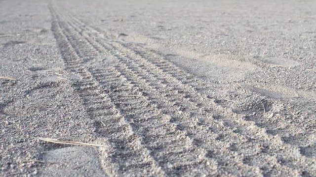 Low angle shot of tire tracks in coarse sand stretching out the edge of the frame.  Slow pan.