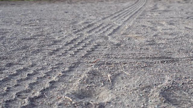 Low angle shot of tire tracks in coarse sand stretching out the edge of the frame.  Slow pan.