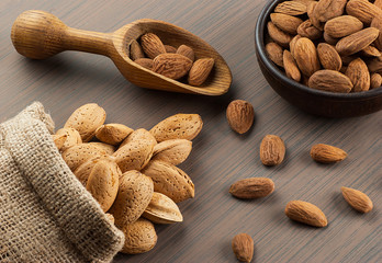 Almonds nuts in dark Brown bowl on rustic vintage wooden table with wooden spoon or scoop and almond shell in burlap sack. Almond background concept with copy space
