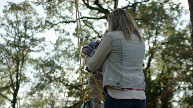 Mom Places Her Little Boy In Swing On A Beautiful Sunny Autumn Day, Slow Motion