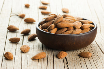 Almonds nuts in dark Brown bowl on rustic vintage wooden table with wooden spoon or scoop . Almond background concept with copy space