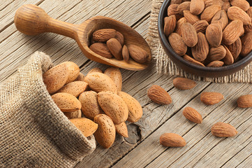 Almonds nuts in dark Brown bowl on rustic vintage wooden table with wooden spoon or scoop and...