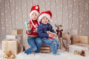 Portrait of white Caucasian happy children brother and sister wearing Santa Claus hats celebrating Christmas. Little cute adorable boy and girl siblings holding caps in studio with holiday decoration