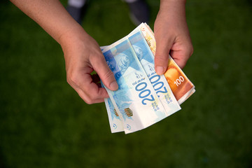 Woman holding a bunch of Israeli New Shekel banknotes in her hands.