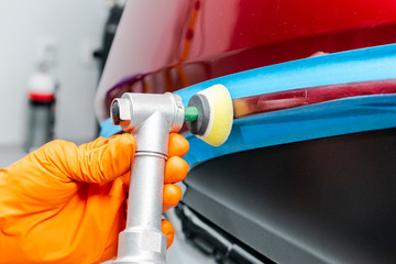 Car polish wax worker hands applying protective tape before polishing. Buffing and polishing car. Car detailing. Man holds a polisher in the hand and polishes the car