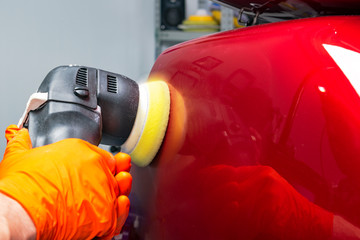 Car polish wax worker hands applying protective tape before polishing. Buffing and polishing car. Car detailing. Man holds a polisher in the hand and polishes the car
