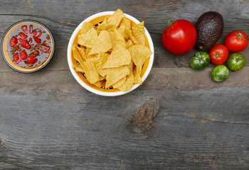 bowls of chips and salsa with tomatoes and an avacado on a rustic table top