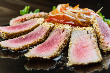 Close Up Still Life of Roasted Tuna Steaks Crusted with Herbs and Sesame Seeds on Dark Gray Surface