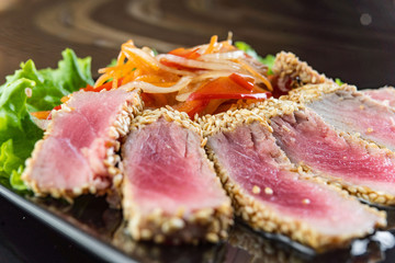 Close Up Still Life of Roasted Tuna Steaks Crusted with Herbs and Sesame Seeds on Dark Gray Surface