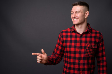 Candid studio shot of young handsome man smiling and pointing finger