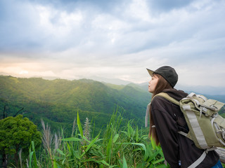 young girl with backpack enjoying sunset on peak mountain. Tourist traveler on background valley landscape view. Hiker looking sunlight flare in trip in Thailand,Kamphaeng Phet Province