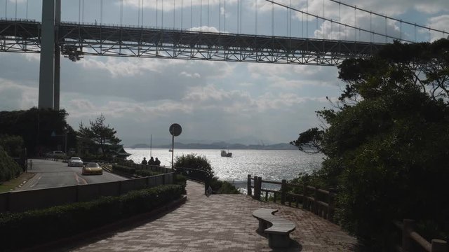 Cars Drive By as a Ship Sails Under the Scenic Kanmon Bridge in Kitakyushu Japan