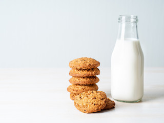 Oatmeal cookies with flax seeds and milk in bottle, healthy snack. Light background, grey light wall