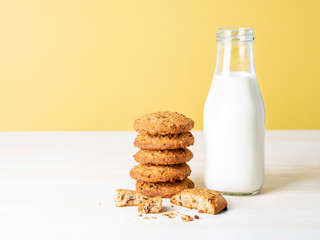 Oatmeal cookies with flax seeds and milk in bottle, healthy snack. Light background, bright yellow wall