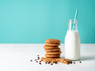 Oatmeal cookies with chocolate drops and milk in bottle, healthy snack. Light background, bright blue wall