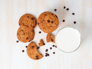 Oatmeal cookies with chocolate drops and milk in glass, healthy snack. Light background, white wooden table, top view