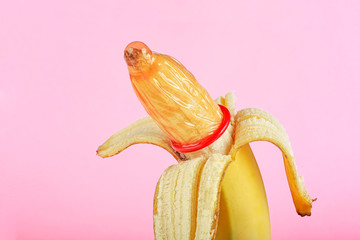 Red condom on yellow banana, pink background.