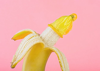 Safe sex concept - yellow condom on banana, pink background.