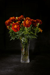 Bouquet of garden flowers marigolds in a glass vase on a black background