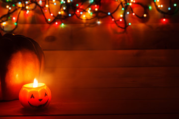 Halloween candle in the dark on a wooden background. Behind the pumpkin in the lights of the garland