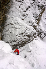 ice climber in red jacket on a steep snow covered icefall in the Swiss Alps