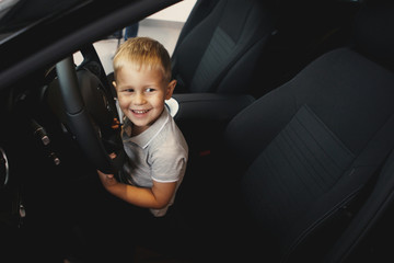 Funny little boy is sitting in the cabin of a new automobile and is happy. Just buy a car in the dealer center. The concept of buying a vehicle.