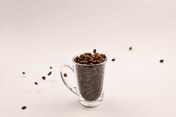 Grains of coffee are poured into a glass cup on a white background