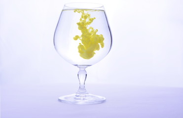 Yellow paint in water in a crystal glass on a white background