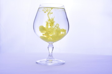 Yellow paint in water in a crystal glass on a white background