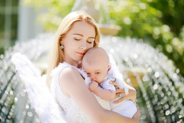 Beautiful mother and her baby son wearing angel costumes. Cheerful moment, loving family.