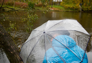 A man under a transparent umbrella on a cloudy autumn day on the lake shore..