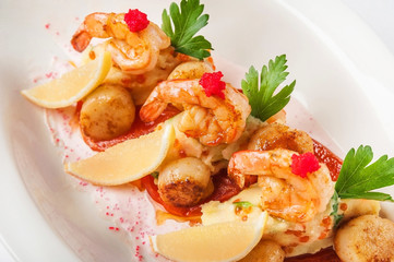 Three shrimps on a pillow of their hummus with scallops and lemon on a white plate. Traditional food shrimp and scallops close up in bright