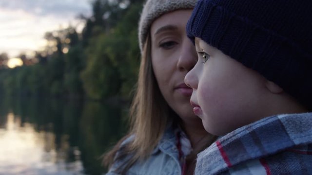 Closeup Of Mother And Little Boy, He Points To The Sky, They Look Up In Wonder, Beautiful Sunset On Waterfront, Slow Motion