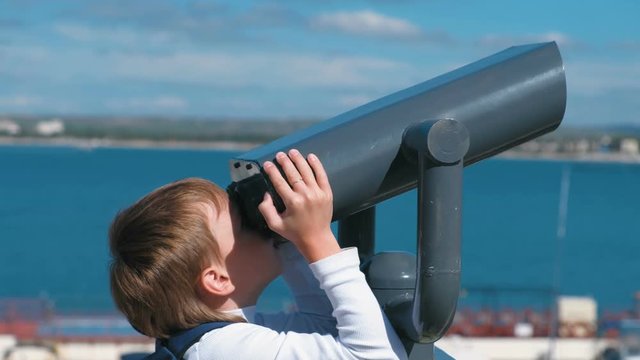 Unrecognizable boy looks through binoculars at the sea.