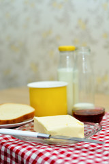 Delicious, warm autumn breakfast - hot milk in a yellow mug, butter, slices of bread and jam.