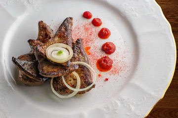 Fried liver with onion, ketchup and chili pepper. Cooked liver in a white plate on a wooden table
