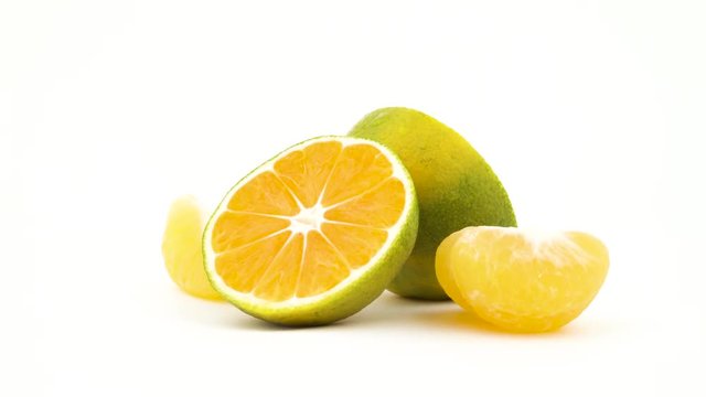 Two halves of a green tangerine fruits with water drops. Green mandarin slices rotating. Isolated on the white background. Close-up. Macro.